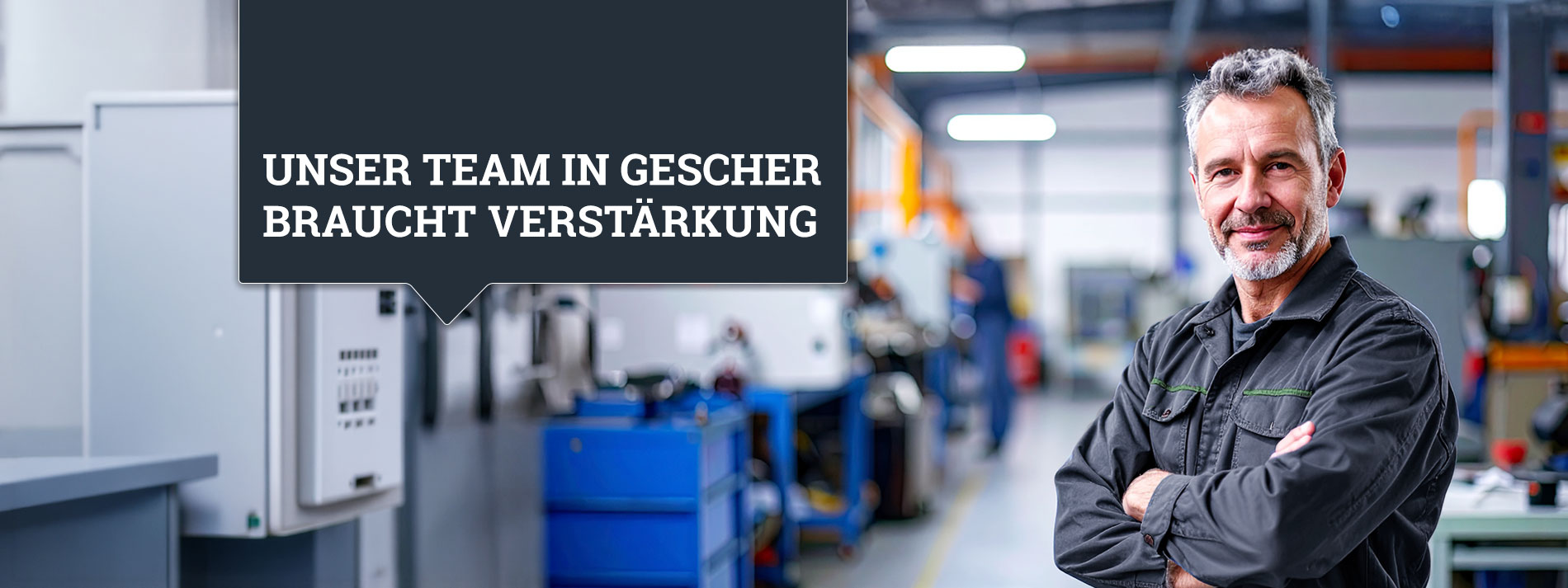 Mann mittleren Alters mit Bart in grauer Arbeitsmontur steht rechts im Bild, Arme verschränkt, Blick in die Kamera. Im Hintergrund eine Werkstatt, unscharf zu sehen.